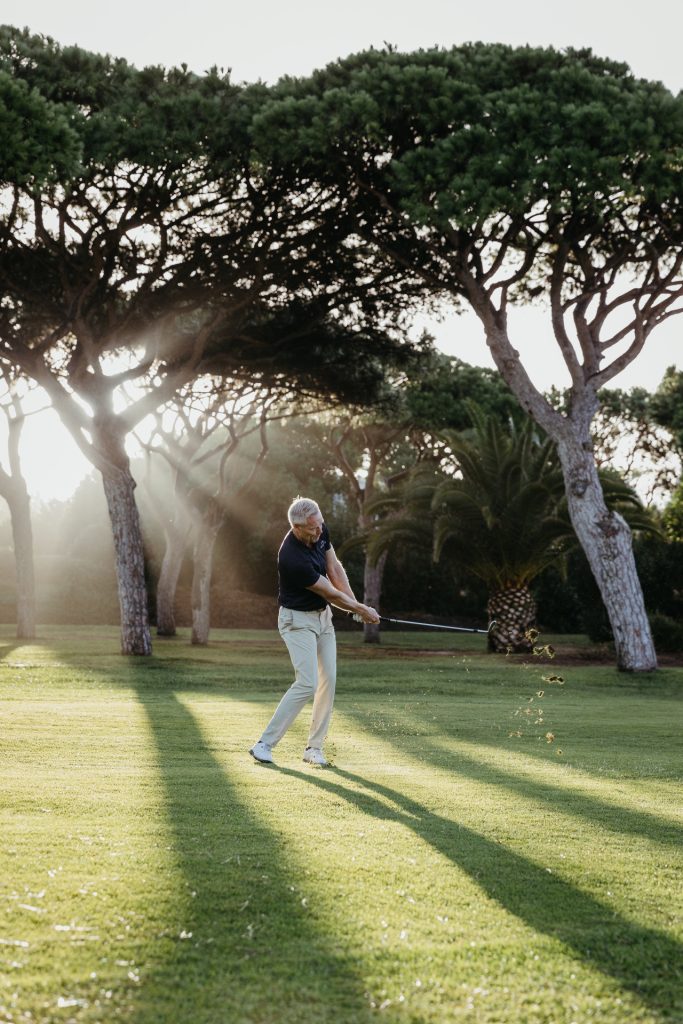 A golfer swinging his club on the green as sunlight filters through the trees at Vale do Lobo Resort.