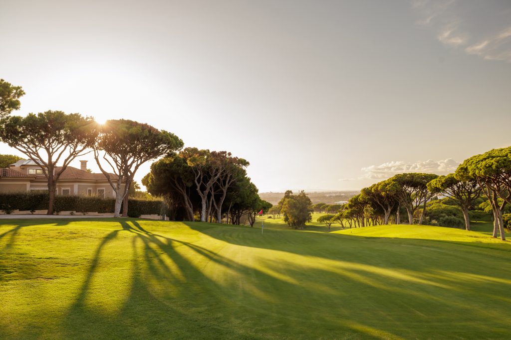 The sun setting over a tranquil golf course with trees casting long shadows at Vale do Lobo Resort.